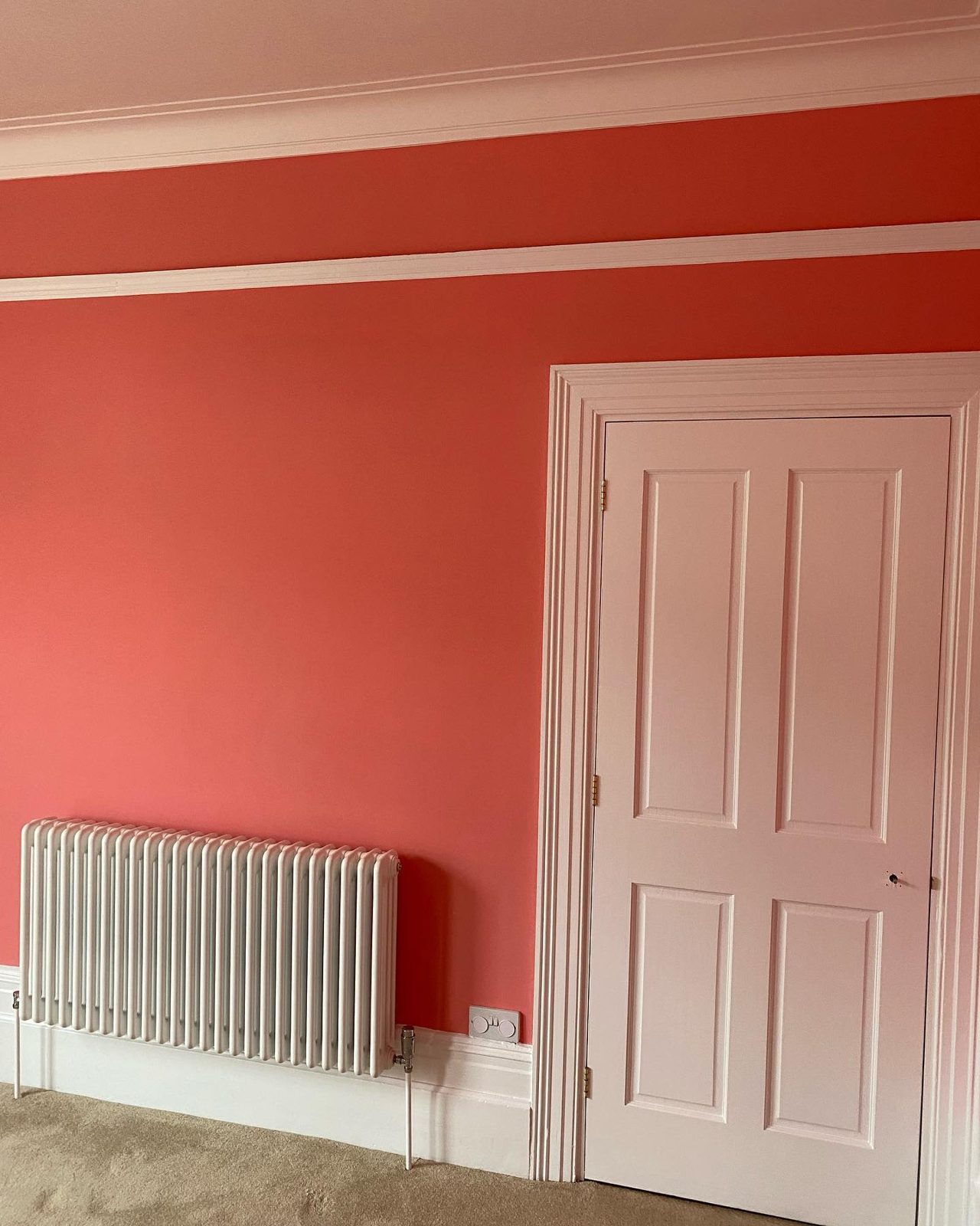 Coral red room with white panelled door, cornice and column radiator in a Victorian house
